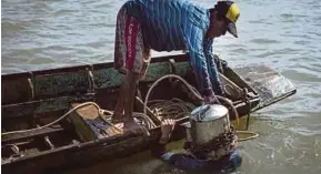  ?? PIC AFP ?? A boatman placing a homemade metal scuba helmet on Somsak Ongsaard before he dives into Chao Phraya river in Bangkok.