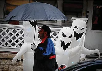  ??  ?? A man tried to protect against the rain while walking past some Halloween decoration­s on Huffman Avenue in Dayton on Wednesday, Oct. 31.