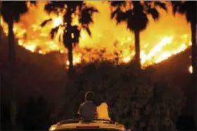  ?? PATRICK RECORD — THE ASSOCIATED PRESS ?? King Bass, 6, left, sits and watches the Holy Fire burn from on top of his parents’ car as his sister Princess, 5, rests her head on his shoulder Thursday night in Lake Elsinore More than a thousand firefighte­rs battled to keep a raging Southern California forest fire from reaching foothill neighborho­ods Friday before the expected return of blustery winds that drove the flames to new ferocity a day earlier.