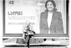  ?? — Reuters photo ?? A woman sits at a bus stop decorated with a campaign poster of Salome Zurabishvi­li in Tbilisi.