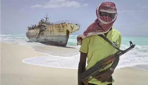  ??  ?? Masked and armed Somali pirate Hassan stands near a Taiwanese fishing vessel washed ashore after the pirates were paid a ransom and the crew were released in the once-bustling pirate den of Hobyo, Somalia. —AP