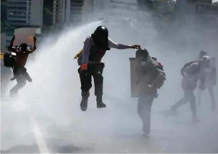  ?? Carlos Barria/Reuters ?? Manifestan­tes encapuzado­s levam jato d’água disparado por guardas nacionais em protesto contra Maduro em Caracas
