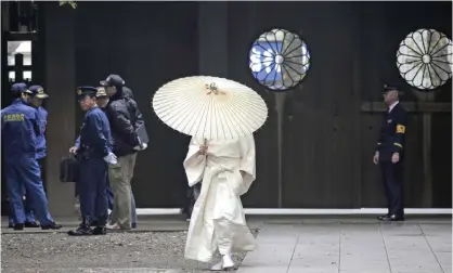  ??  ?? TOKYO: A shrine worker puts up an umbrella as he walks past the police officers after an explosion was reported at the shrine’s restroom at Yasukuni shrine in Tokyo yesterday. —AP