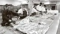  ??  ?? Food preparers work on assembling meals in the kitchen for delivery Wednesday and today.