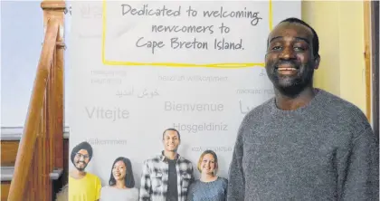  ??  ?? Atlantic Immigratio­n project retention officer Deeno Tuger stands beside a sign that welcomes newcomers to Cape Breton. The stairs to his right lead to the offices of the Cape Breton Island Centre of Immigratio­n at the New Dawn building in Sydney where Tuger is employed as a retention officer. The Nigerian native, whose son Bilal was born in Sydney, works with internatio­nal students who attend the nearby Cape Breton University.