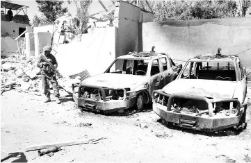  ??  ?? A member of the Afghan security forces stands guard next to damaged army vehicles after a Taliban attack in Ghazni city, Afghanista­n. — Reuters photo