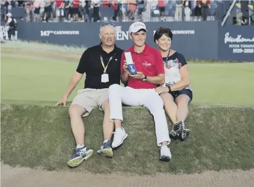  ??  ?? 0 Sam Locke perches on the edge of the 18th green with his parents and holds his silver medal for finishing best amateur at Carnoustie