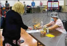  ?? ASSOCIATED PRESS 2020 ?? Election worker Adonlie DeRoche (seated) works behind plexiglass for safety while handing a ballot and single-use pen to a voter during the primary election in Portland, Maine.