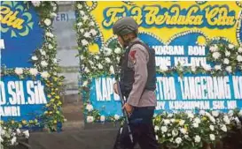  ?? EPA PIC ?? A policeman in front of a wreath of flowers near a bus station damaged by the bomb blasts in Jakarta yesterday.