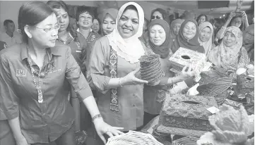  ??  ?? Shahrizat takes a close look at a handicraft item made by an artisan from Kampung Sg Buloh. She is accompanie­d by Minister in the Prime Minister’s Department Nancy Shukri (on her left). - Photo by Muhammad Rais Sanusi