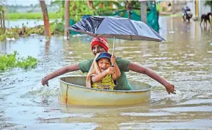 ??  ?? A man and a child wade through a flooded road after heavy rain in Nagercoil