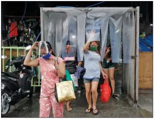  ?? (AP/Aaron Favila) ?? Women leave a disinfecti­ng area Monday after stocking up at a Quezon, Philippine­s, market ahead of stricter lockdown measures. Philippine President Rodrigo Duterte is reimposing a moderate lockdown in the capital and outlying provinces after medical groups appealed for the move as coronaviru­s infections surge. More photos are available at arkansason­line.com/84virus/