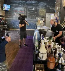  ?? T.J. Fairchild ?? Hemi Braunstein, Commonplac­e Coffee's service manager, standing behind the counter, and Tipsy Bean owner, Gisele Littrell, kneeling next to him, are filmed by the Discovery Channel crew for "Undercover Billionair­e Comeback City."