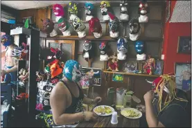  ??  ?? Lucha Libre brothers “Ciclonico” (left) and Mister Jerry eat at their restaurant that also sells fighter masks in Xochimilco. While wrestling halls are closed amid the covid-19 pandemic, they now make their livings selling flowers they grow on Xochimilco’s artificial islands, known as chinampas, and selling tacos and tortas.