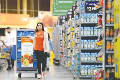  ?? FILE PHOTOS BY JULIO CORTEZ/THE ASSOCIATED PRESS ?? Laila Ummelaila, a personal shopper at a Walmart store in Old Bridge, N.J., pulls a cart with bins as she shops for online shoppers. Personal shoppers collect items on online orders and greet customers at a pickup location in the parking lot.