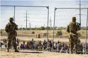  ?? ASSOCIATED PRESS ?? Migrants wait in line near the border fence at El Paso, Texas, under the watch of the Texas National Guard, on May 10.