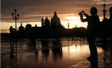  ?? GETTY IMAGES ?? RAIN, RAIN: A woman take a picture at the sunset in Venice, during ‘acqua alta,’ or high water, of over 5 feet on Sunday. Below left and right, people go to a bar amid rising water in Venice.