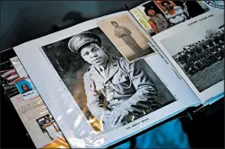  ??  ?? Primm holds up a scrapbook with pictures of his service in World War II as he speaks about his time serving.