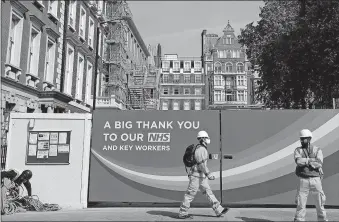  ?? [KIRSTY WIGGLESWOR­TH/ THE ASSOCIATED PRESS] ?? A constructi­on worker passes a sign thanking the NHS on Thursday in London as the country is in lockdown to prevent the spread of the coronaviru­s.