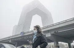  ?? BLOOMBERG ?? A morning commuter walks near the CCTV tower in Beijing amid smoggy conditions on Nov 5.