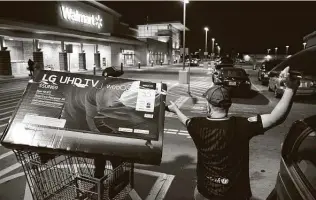  ??  ?? Wilber Guevara, right, and stepson Rodrigo Garcia load a television into their car on Black Friday in Dallas. Guevara said this was his first time for Black Friday shopping and described it as calm.