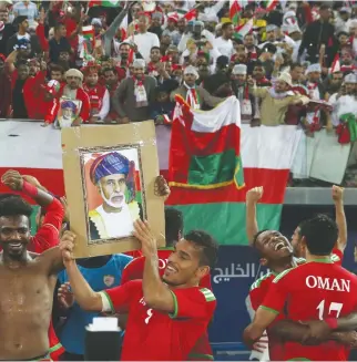  ??  ?? Oman’s players hold a picture of Oman’s Sultan as they celebrate with their fans after winning the Gulf Cup semi-final with Bahrain. (AFP)