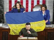  ?? AP ?? VP Kamala Harris and then-House Speaker Nancy Pelosi react as Volodymyr Zelenskyy presents lawmakers with a Ukrainian flag autographe­d by front-line troops.