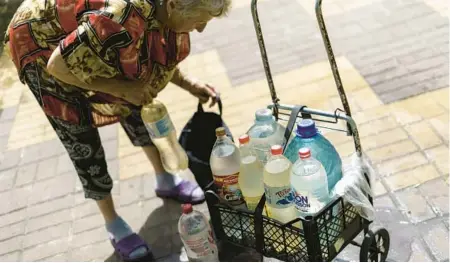  ?? DAVID GOLDMAN/AP ?? Lyubov Mahlii, 76, packs a crate with water bottles she filled at a public tank to take back to her apartment in Sloviansk, Ukraine on Aug. 6.