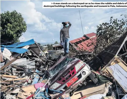  ?? Carl Court ?? &gt; A man stands on a destroyed car as he views the rubble and debris of destroyed buildings following the earthquake and tsunami in Palu, Indonesia