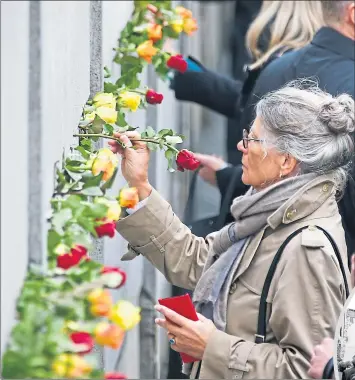  ??  ?? People place flowers in gaps of the last part of the Berlin Wall at Bernauer Strasse