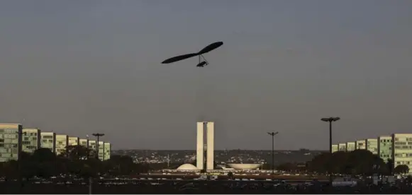  ??  ?? A hang glider flies over modernist buildings gracing Three Powers Square in Brasilia. But tough times are coming for public-sector workers as the bureaucrac­y shrinks in the capital city.