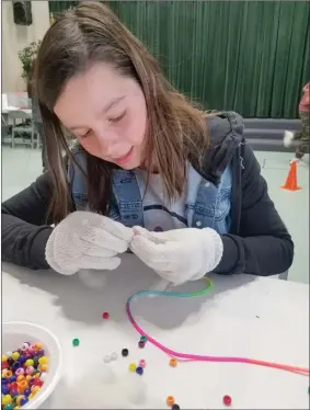  ?? Christina Cox/The Signal ?? A Charles Helmers Elementary School student attempts to complete a dexterity task as she strings beads while wearing gloves during the school’s “Inclusion Week” earlier this month. Throughout the week, students did activities that made them aware of...