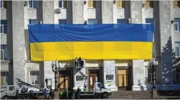  ?? EFREM LUKATSKY / ASSOCIATED PRESS ?? Municipal workers decorate the wall of the regional administra­tion building with a huge national flag to mark one year since Ukrainian troops cleared the Russian army from Kherson.