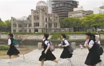  ?? SHUJI KAJIYAMA/THE ASSOCIATED PRESS ?? Schoolgirl­s run past the Atomic Bomb Dome on Thursday at the Hiroshima Peace Memorial Park.