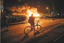  ?? Brandon Bell / Getty Images ?? A man sits on a bike while watching a used car lot burn in Kenosha, Wis., during a second night of civil unrest.