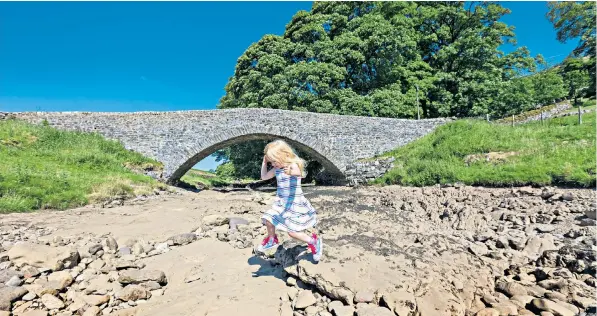  ??  ?? A young girl plays on the dried-up riverbed of the Wharfe in the village of Yockenthwa­ite, N Yorks, as the heatwave parching Britain shows little sign of abating. Forecaster­s say the dry spell could continue for up to a month