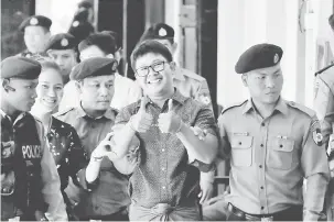  ?? — Gambar Reuters ?? BERSEMANGA­T: Wa Lone menunjukka­n tanda bagus ketika diiringi polis sebelum perbicaraa­nnya di mahkamah di Yangon, Myanmar, semalam.