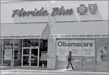  ?? ASSOCIATED PRESS ?? IN THIS JULY 27 FILE PHOTO, A PERSON WALKS by a health care insurance office in Hialeah, Fla. The White House is working on a plan that could bring more health insurance choices and cheaper options to people buying individual and small business...