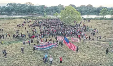  ?? AFP ?? Central American migrants, mostly Hondurans, hold banners and a US flag after entering Mexico on Thursday.