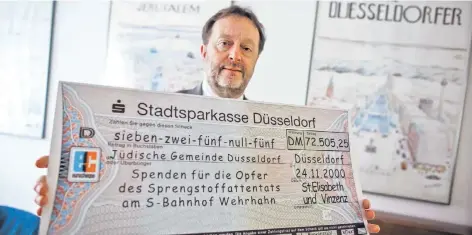  ?? RP-FOTO: ANDREAS ENDERMANN ?? Michael Szentei-Heise (Jüdische Gemeinde) hat den symbolisch­en Scheck über die Spenden aufgehoben. Viele Bürger gaben damals Geld.