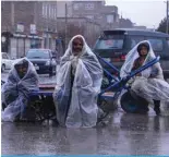  ?? ?? HERAT: Afghan workers cover themselves with the plastic sheets during the rainfall as they sit on their hand carts along a road in Herat on March 12, 2024. — AFP