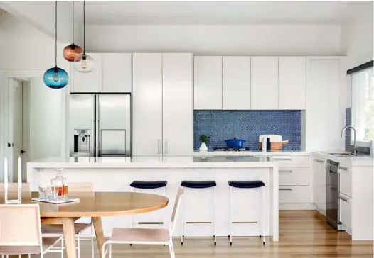  ??  ?? KITCHEN AND DINING Interior decorator Sarah Elshaug of The Retreat Stylist introduced the stunning glazed pendants (above) from Mark Douglass Design in Steel Blue, Aubergine and Clear, along with the retro penny round mosaic tiles in Indigo from Byzantine Design that line the splashback. “The minute Sarah showed them to us, we knew they were the ones,” says Christine. A trio of ‘Dita’ stools in Navy and White from Grazia & Co draw the home’s favoured accent colour into the cooking zone, too. Centred by a bespoke oak table from Arthur G, and ‘Boston’ leather chairs in Rose Blush from Barnaby Lane, the designated dining zone adjacent to the kitchen flows through into the outdoor area (below), where the family (pictured from left Pippa, Christine, Richard, Olivia and Charlotte) love to gather for meals and play.