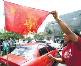  ?? (AFP FOTO) ?? BURNING RED. Anti-China activist and former policeman Abner Afuang burns a Chinese flag during a protest in front of the Department of Foreign Affairs building in Manila.