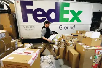  ?? AP PHOTO ?? Package handler Chris Addison arranges packages before loading a delivery truck at a FedEx sorting facility