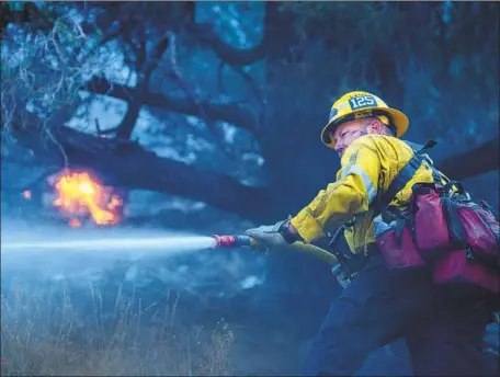  ?? Allen J. Schaben Los Angeles Times ?? L.A. COUNTY firefighte­r Tommy Davis douses a hot spot Sunday as the Bobcat fire burns in the northern Angeles National Forest hills.