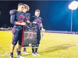 ?? ADAM LICHTENSTE­IN/SUN SENTINEL ?? Three Stoneman Douglas football players prepare to present former coach Aaron Feis’ family with his retired jersey. The Eagles honored the victims of the February mass shooting at halftime of their game against Taravella on Thursday.