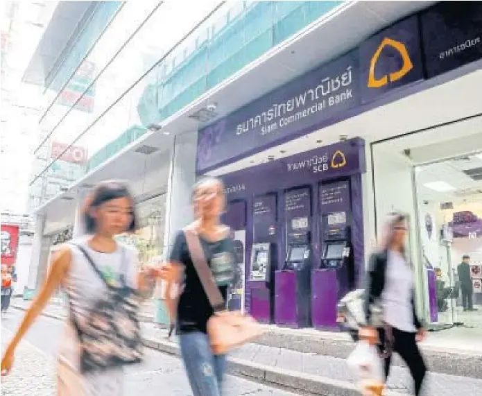  ??  ?? PAYING A PRICE: People walk past a branch of Siam Commercial Bank (SCB) in central Bangkok. SCB is set to downsize over the next three years as it embraces changes brought on by the digital banking era. It has announced plans to close down more than...