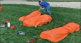  ?? CONTRIBUTE­D PHOTO ?? Three contractor­s successful­ly deployed in the orange plastic practice fire shelters. The instructor is checking each one to be sure the shelter fabric is tightly held to the ground by the feet and arms. When they crawl out of the shelters, they then have to carefully fold and repack them in the bags and boxes just thrown down near their feet for the next guy or gal. Though you can’t tell it, the middle shelter in this picture was covering a young lady.