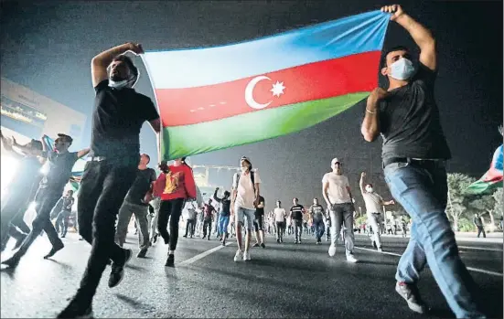  ?? AZIZ KARIMOV / AP ?? Dos hombres portan la bandera nacional durante una manifestac­ión en apoyo al ejército de Azerbaiyán en Bakú