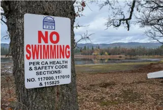  ?? Maggie Beck / Union Democrat ?? A sign (above) posted near Phoenix Lake warns people to not swim in the reservoir. Boats (below) sit on the shore of Phoenix Lake Thursday morning.